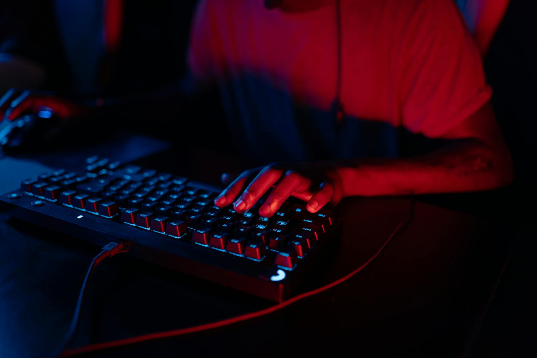 Focus on hands typing on an RGB gaming keyboard under ambient red and blue lighting. on Frame Rate Vault