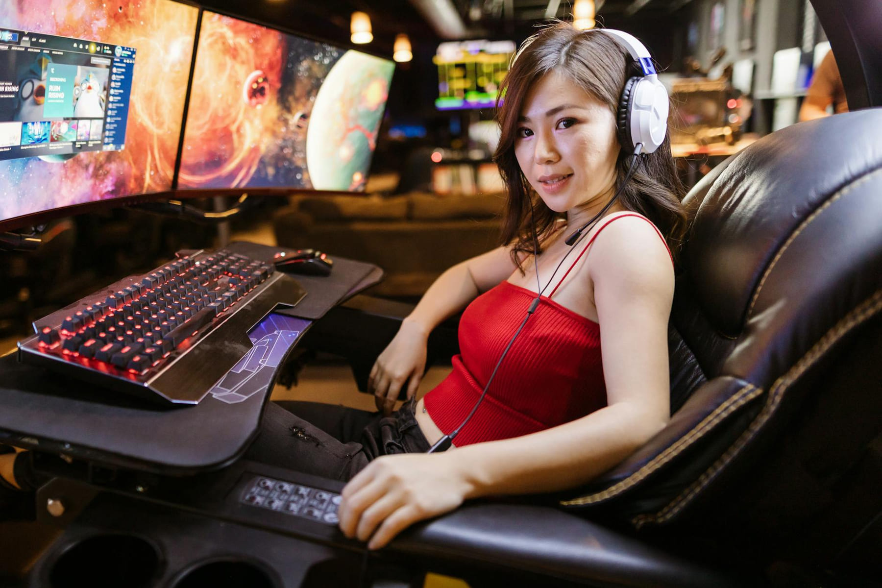A woman engaged in gaming at a high-tech setup with dual monitors and white headphones. on Frame Rate Vault