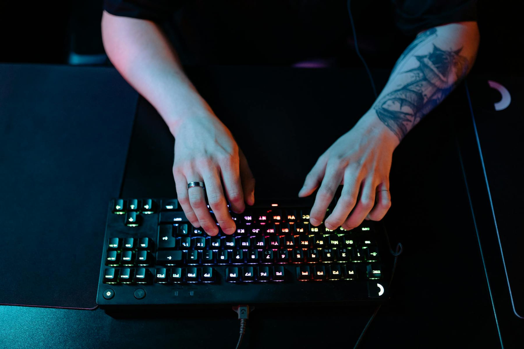 Close-up of hands typing on a RGB gaming keyboard with a tattooed arm and ring visible. on Frame Rate Vault